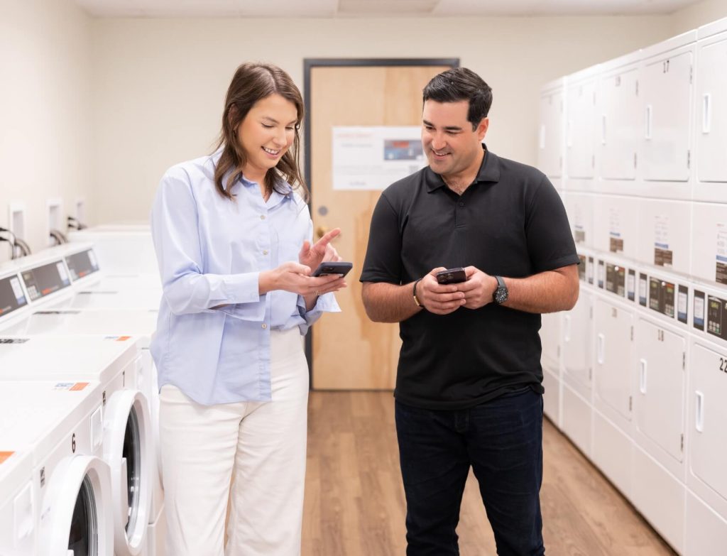 training-inline Two people using Speed Queen technology on phones in room of laundry equipment